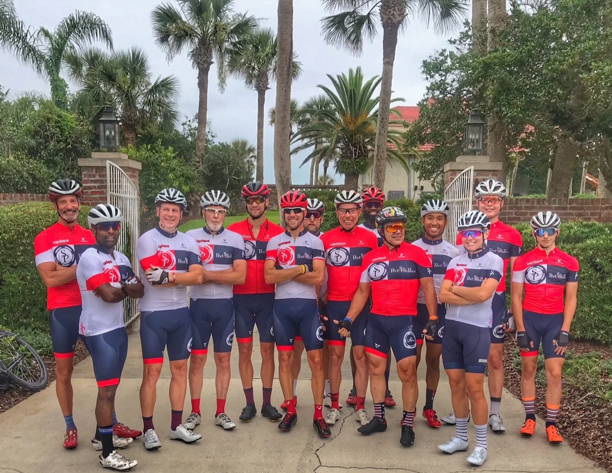 The Shott Performance group ride team in matching red, white, and navy kit, posed at a Ponte Vedra gate before a ride.