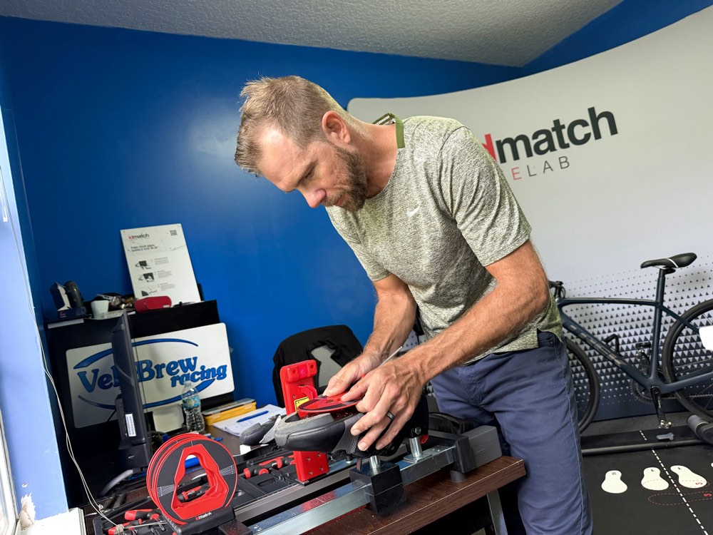 Fitter mounting a cycling shoe in the red IDmatch cleat-fit jig on the workbench.
