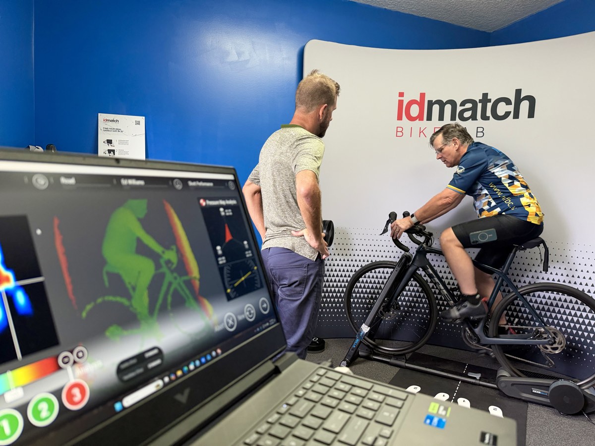 Laptop showing a live IDmatch pressure map and rider silhouette while an athlete pedals on the trainer during a fit.