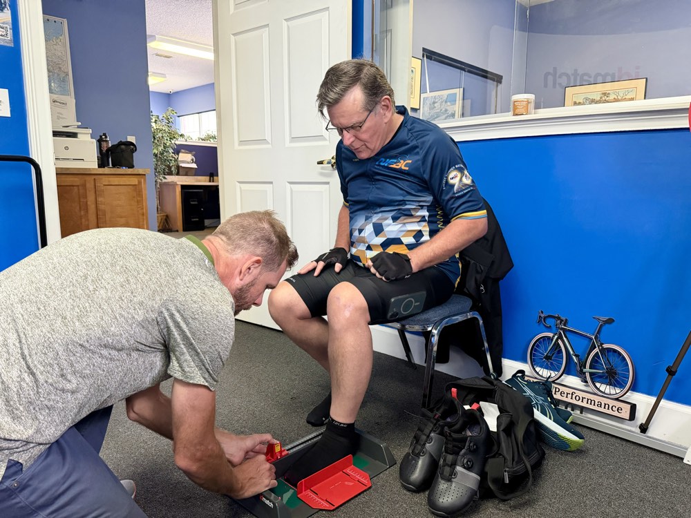 Fitter measuring a seated rider's foot on the red IDmatch foot-measurement device during a bike fit.